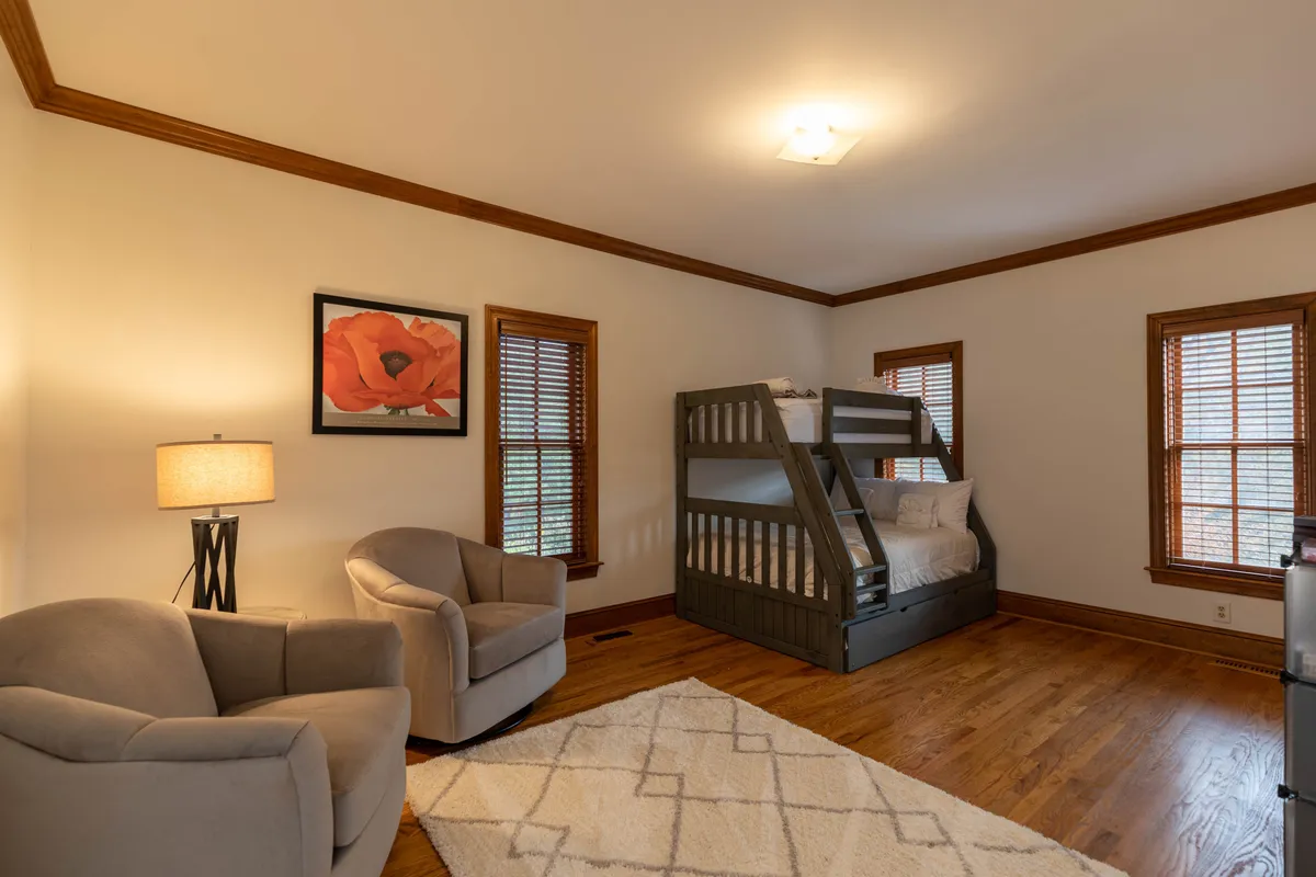 A cozy bunk room with a sturdy bunk bed, two inviting armchairs, a soft lamp, and whimsical artwork on the wall. The space feels playful yet restful, ideal for kids or adults looking for a fun, private nook.