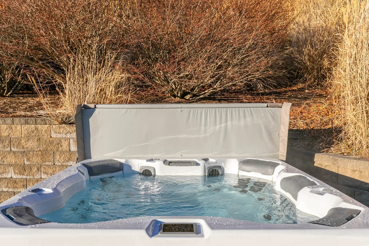 A secluded hot tub set against a stone wall, embraced by lush vegetation. The space feels private and tranquil, suggesting relaxation and intimate moments, like soaking under the stars and sharing stories after a day of fun.