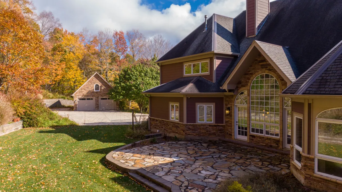 The stone patio, framed by large windows and autumn foliage, invites guests to relax outside. The detached garage hints at ample space for gear after a day spent exploring nearby trails.