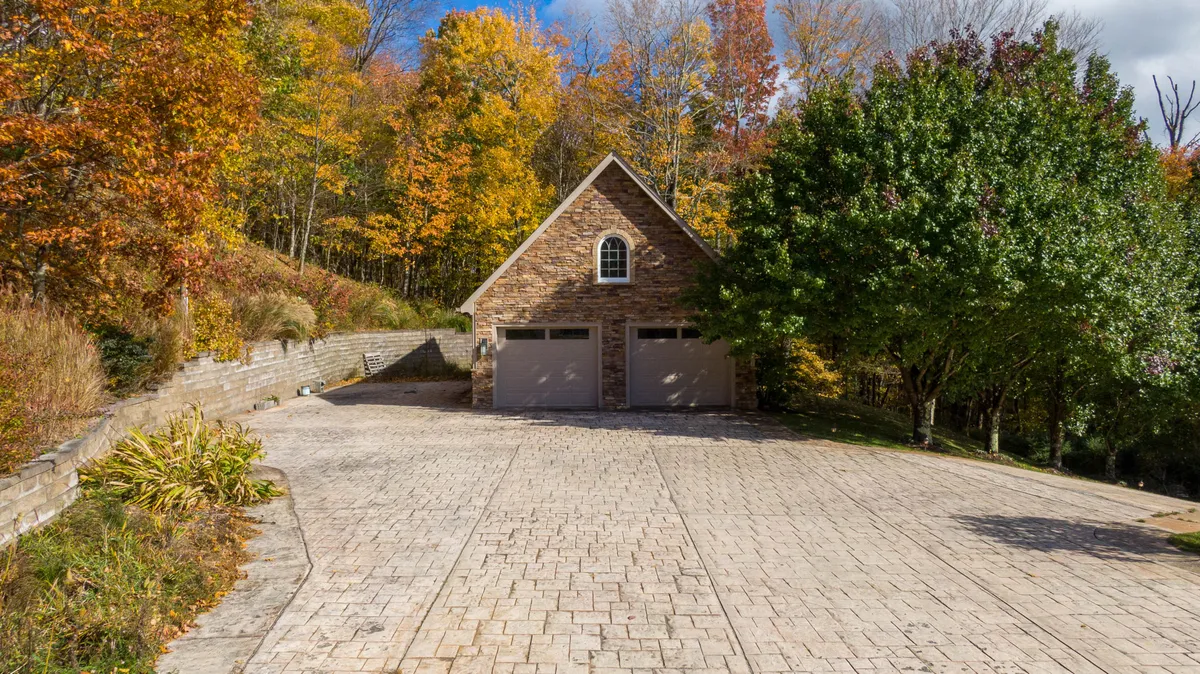 The property’s stone garage and paved driveway are framed by vibrant autumn foliage, with landscaped edges hinting at the care taken in maintaining the outdoor spaces. The scene highlights the seasonal color and ease of access for guests.
