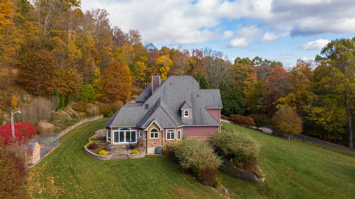 A tranquil view of the house set amidst a beautifully landscaped garden, surrounded by tall trees. The inviting porch and peaceful setting suggest plenty of space for pets to relax or for families to gather outdoors.
