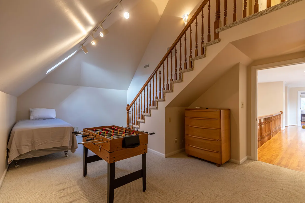 A flexible sleeping area featuring a bed next to a foosball table and a wooden staircase. The playful mood and presence of games suggest a loft or bonus room ideal for families, teens, or friends who want both privacy and entertainment.