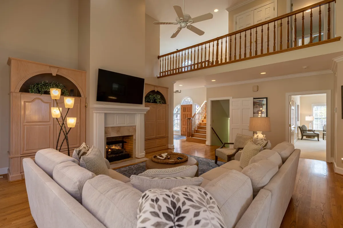A cozy living room scene featuring a plush sofa, a crackling gas fireplace, a large mounted TV, decorative lighting, and a staircase. The space feels warm and inviting—ideal for movie nights, fireside chats, and group relaxation.
