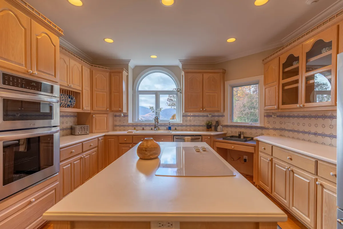 A welcoming kitchen with a prominent central island topped with a decorative bowl, surrounded by wood cabinetry and bar seating. Large windows offer scenic views, and the layout encourages both cooking and casual conversation.
