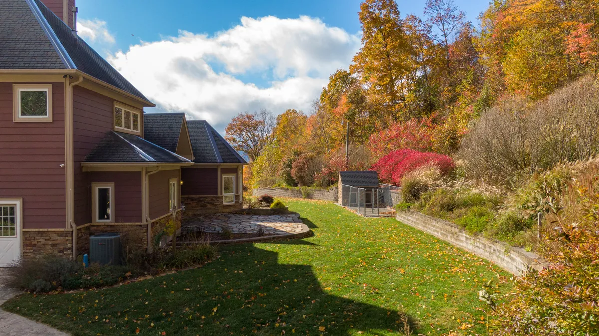 A tranquil view of the house’s facade, surrounded by a landscaped garden and colorful trees. The setting suggests opportunities for gardening, gatherings, and peaceful moments in nature, showcasing the property’s connection to the outdoors.