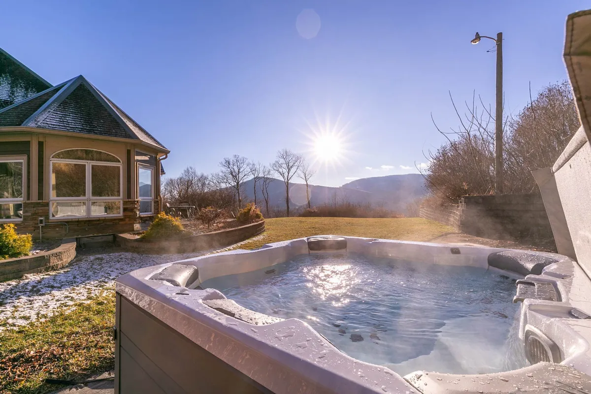 This exterior image captures the inviting hot tub on the stone patio, set against sweeping mountain views. Sunlight bathes the area, and the surrounding landscape hints at the property's peaceful seclusion and elevation.