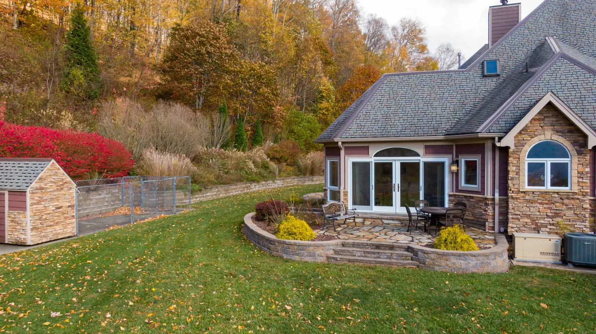 A welcoming stone patio with glass doors opening to the interior, surrounded by colorful fall foliage. The patio is designed for outdoor dining and relaxation, hinting at evenings under the stars and group gatherings with nature as the backdrop.